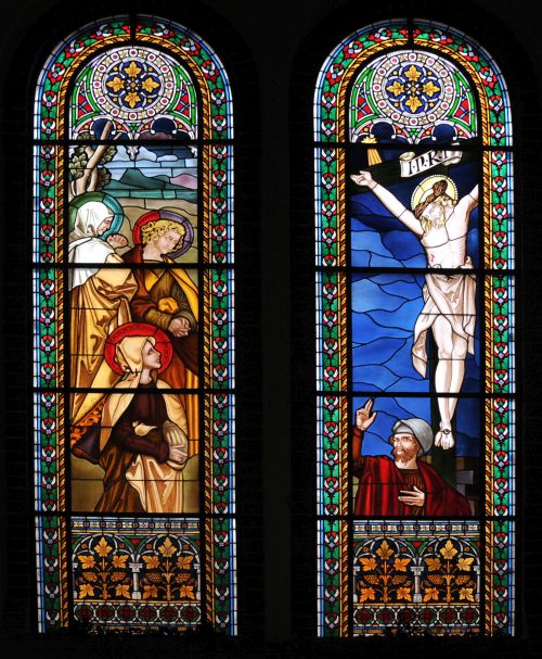 Abbildung: Es sind zwei hohe schlanke Fenster aus farbigem Glas, oben mit Rosetten abgeschlossen. Sie zeigen die Kreuzigung Christi und die Freude über seine Auferstehung.