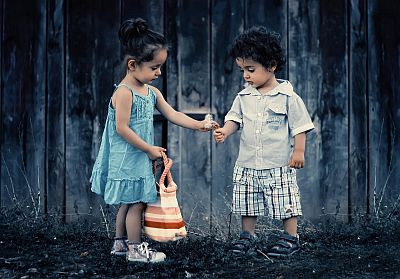 Zwei kleine Kinder, ein Mädchen und ein Junge, stehen beieinander und bestaunen einen kleinen Blumenstrauß. Der Titel des Fotos sagt, dass es Zwillinge, also Geschwister sind.