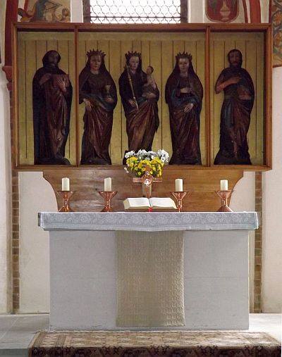 Altar der St. Johanniskirche Foto: Altar mit Steinsockel und -tisch sowie einem dreiflügligen Aufbau aus Kästen. in denen vor goldenem Hintergrund fünf geschnitzte Figuren stehen