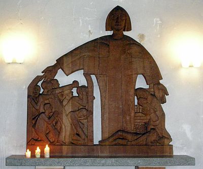 Ehrenmal für die Opfer von Krieg und Gewalt (Lohrisch) Foto einer geschnitzten Altarfigur: Der segnende Christus, in dessen Körper das Kreuz erscheint, breitet seine Arme über eine Gruppe verzweifelt betender und protestierender Menschen, einen Toten und eine der Gottesmutter Maria ähnlichen Frau mit einem Baby.