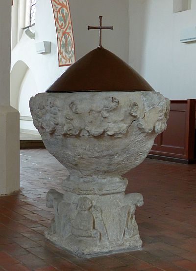 Taufstein der St. Johanniskirche Foto: ein zirka 1 Meter hoher kelchförmiger Taufstein aus Stein. Auf seiner runden Öffnung sitzt eine kegelförmige bronzene Haube mit einem schlichten Kreuz.